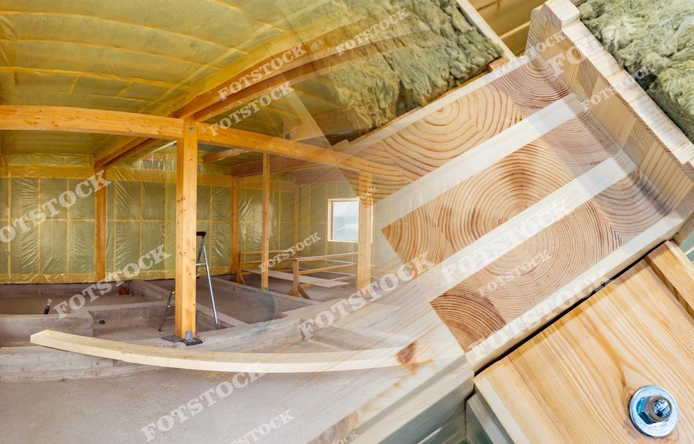 Фотография показывает строительный каркас из деревянных балок с элементами утеплителя на этапе возведения дома. Совмещение натуральной древесины и современных материалов символизирует энергоэффективность и экологичность строительства. В кадре видна структура стен и пола здания.
